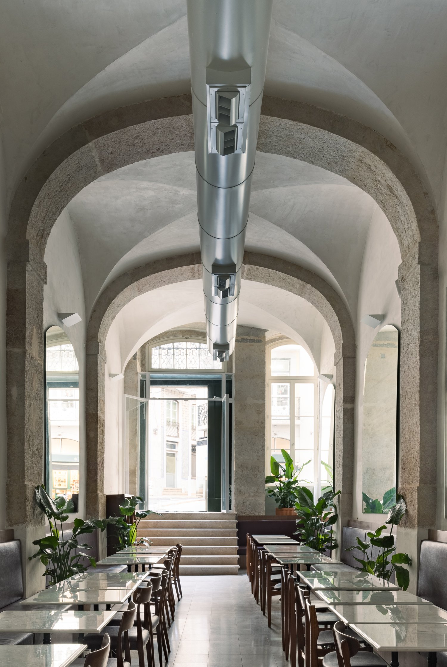 Elegant dining corridor with vaulted ceilings, stone arches, and rows of glass-top tables